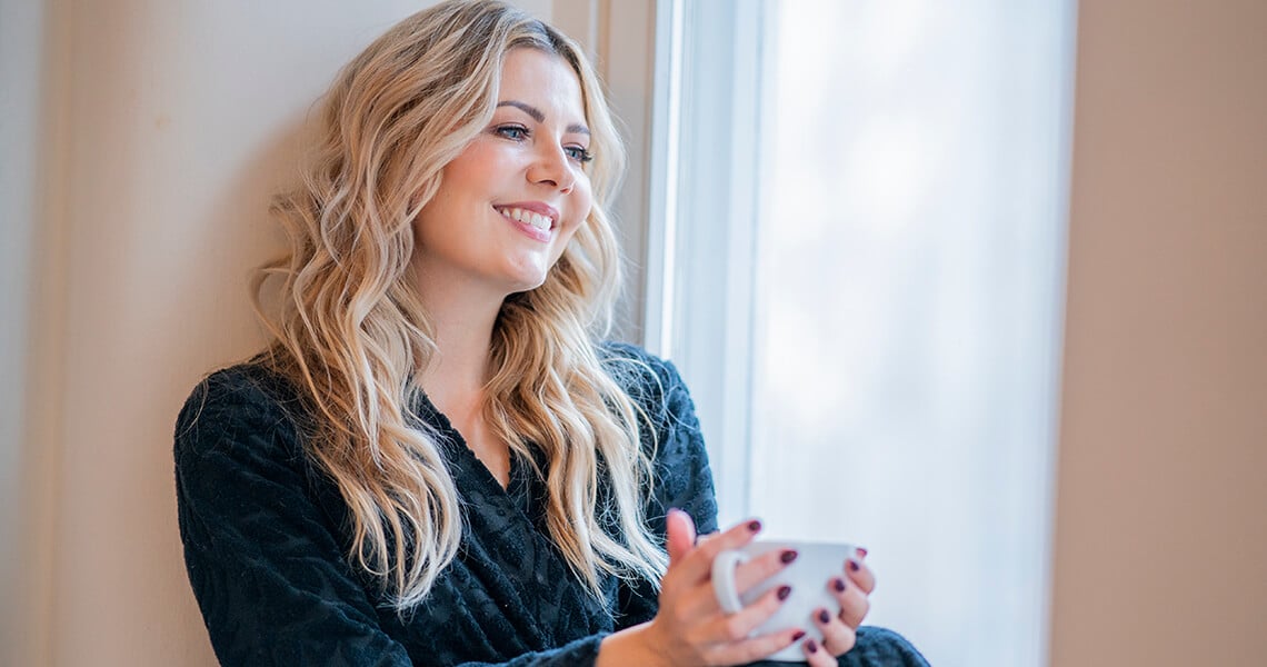 Jenni Alexandrova istuu ikkunalaudalla kylpytakissa kahvikuppi kädessään