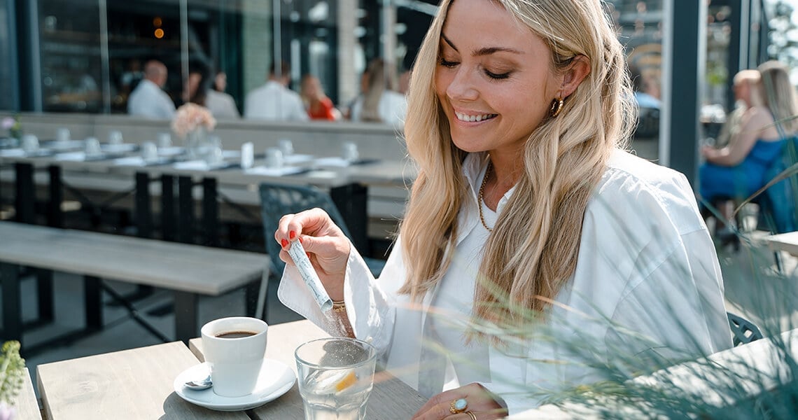 Vaalea hiuksinen nainen kahvilassa sekoittaa annospussin The Solutionia veteen